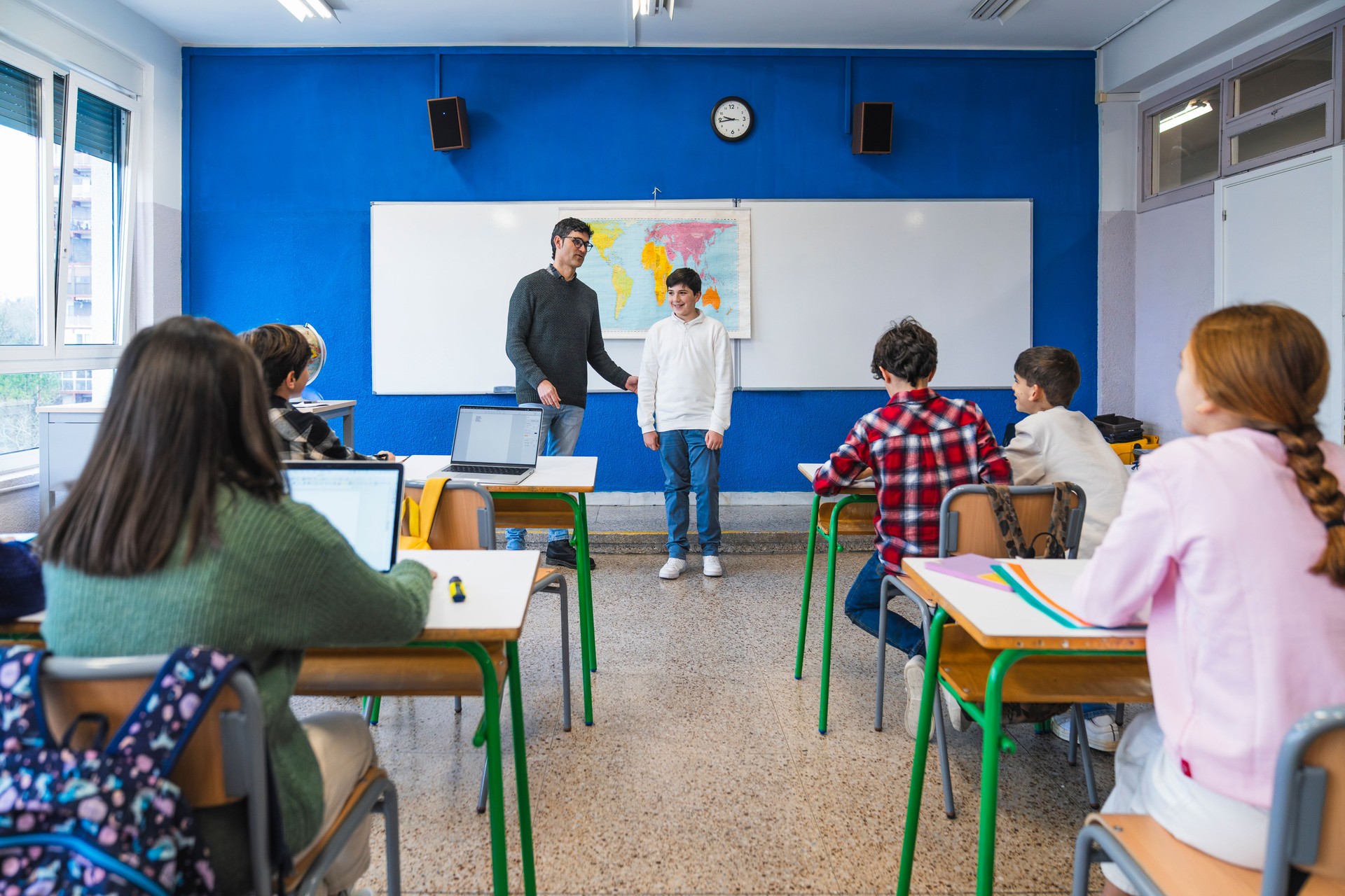 Teacher helping student during geography lesson in classroom